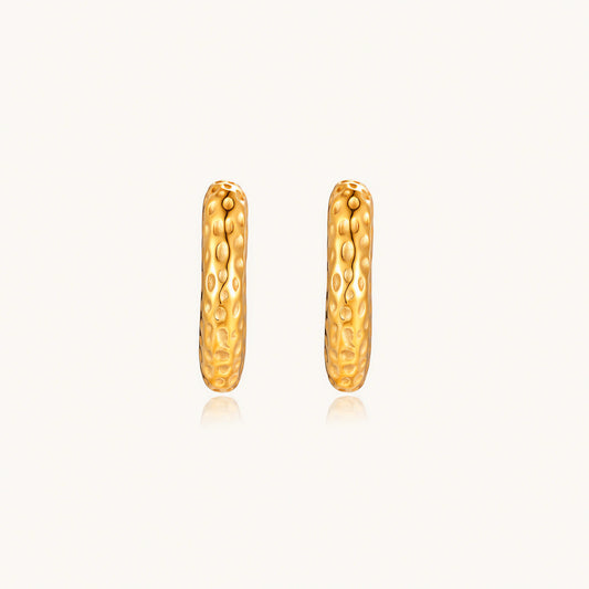 Gold-toned hoop earrings with hammered dimpled texture and post closure on cream background