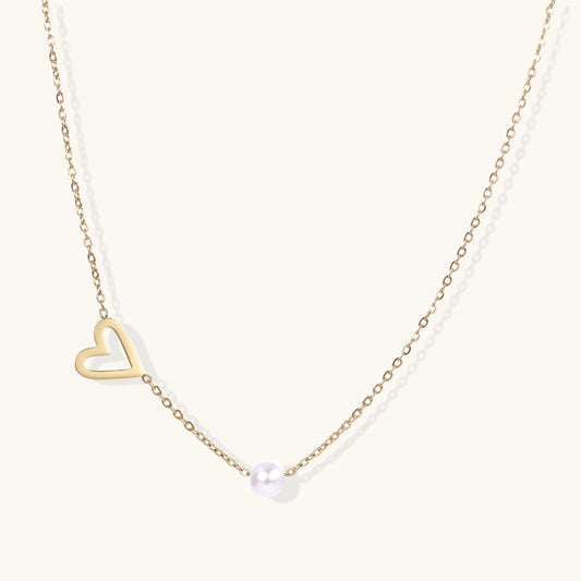 Delicate gold necklace with open heart charm and white pearl bead on fine chain against cream background