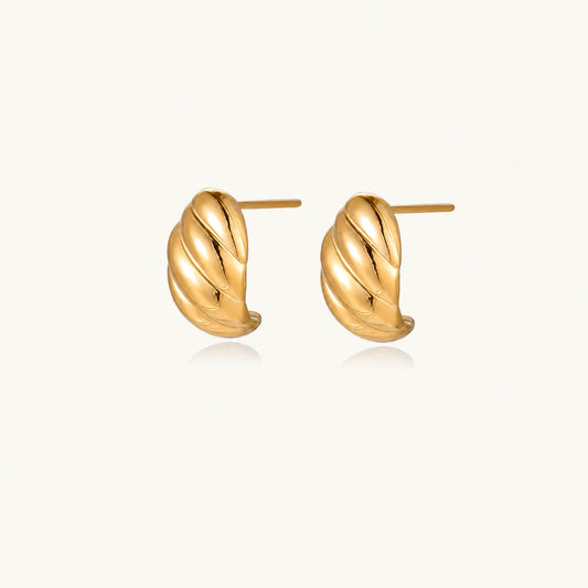 Chunky gold twisted rope huggie hoops with diagonal grooves and high-polish finish on cream background