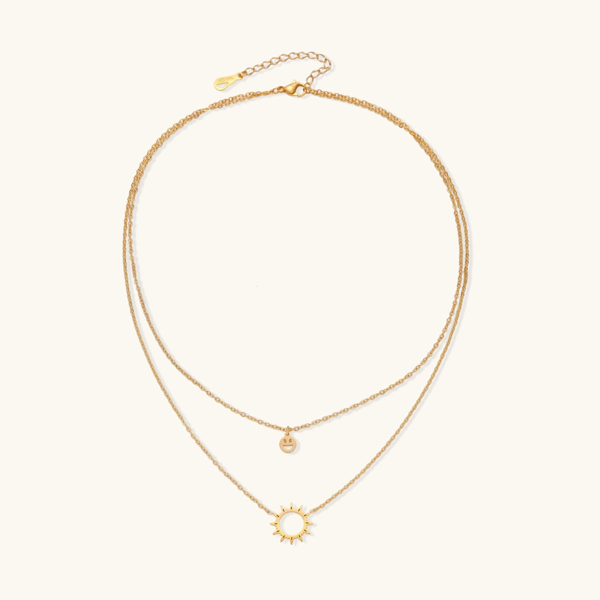 Gold layered necklace set with sunburst and smiley face pendants on delicate chains against white background.