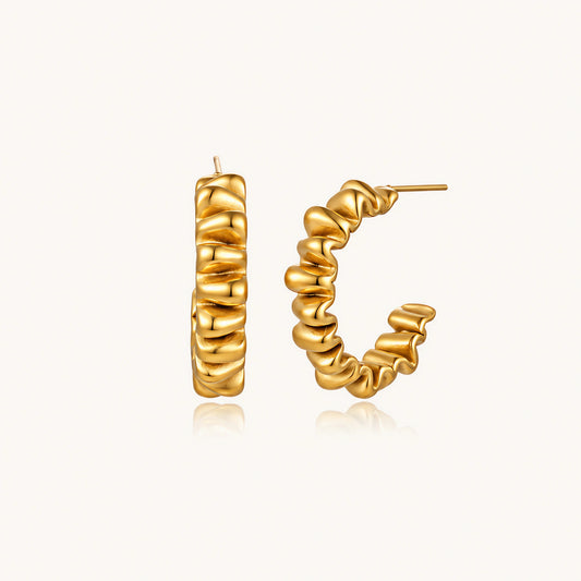 Sculptural gold-plated hoop earrings with continuous twisted spiral design on cream background