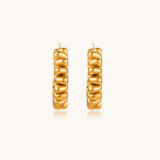 Sculptural gold-plated hoop earrings with continuous twisted spiral design on cream background