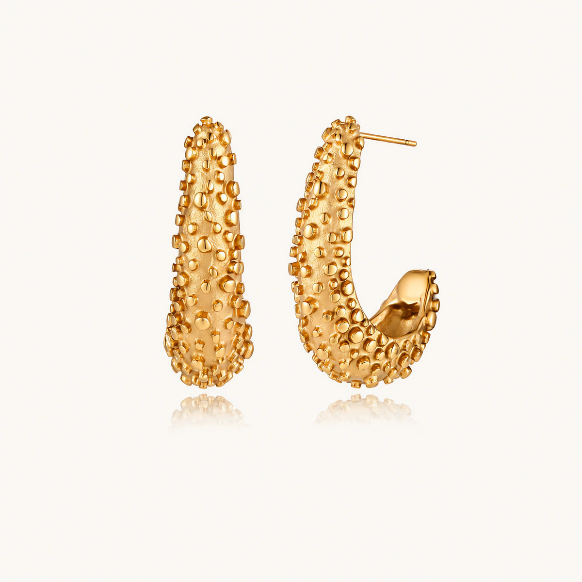 Curved gold hoop earrings with raised granulated texture resembling sea urchin surface on cream background
