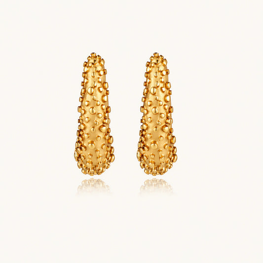 Curved gold hoop earrings with raised granulated texture resembling sea urchin surface on cream background
