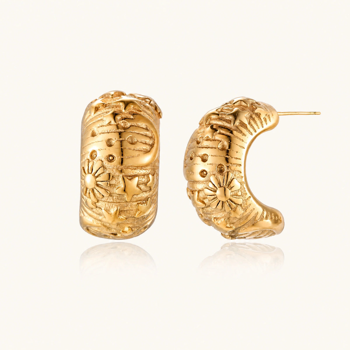 Wide gold hoop earrings with embossed stars and sun motifs on cream background, showing dimensional relief details.
