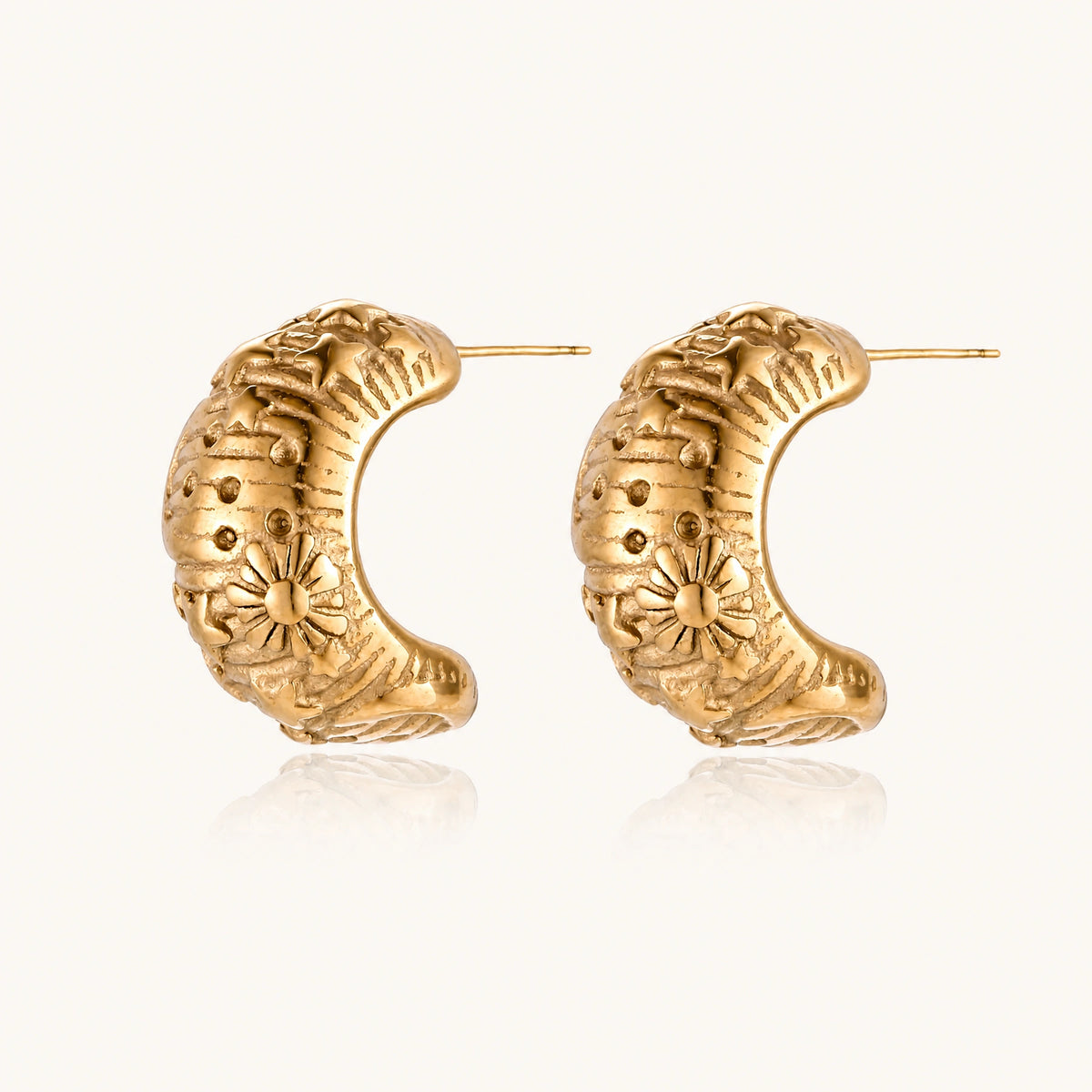 Wide gold hoop earrings with embossed stars and sun motifs on cream background, showing dimensional relief details.