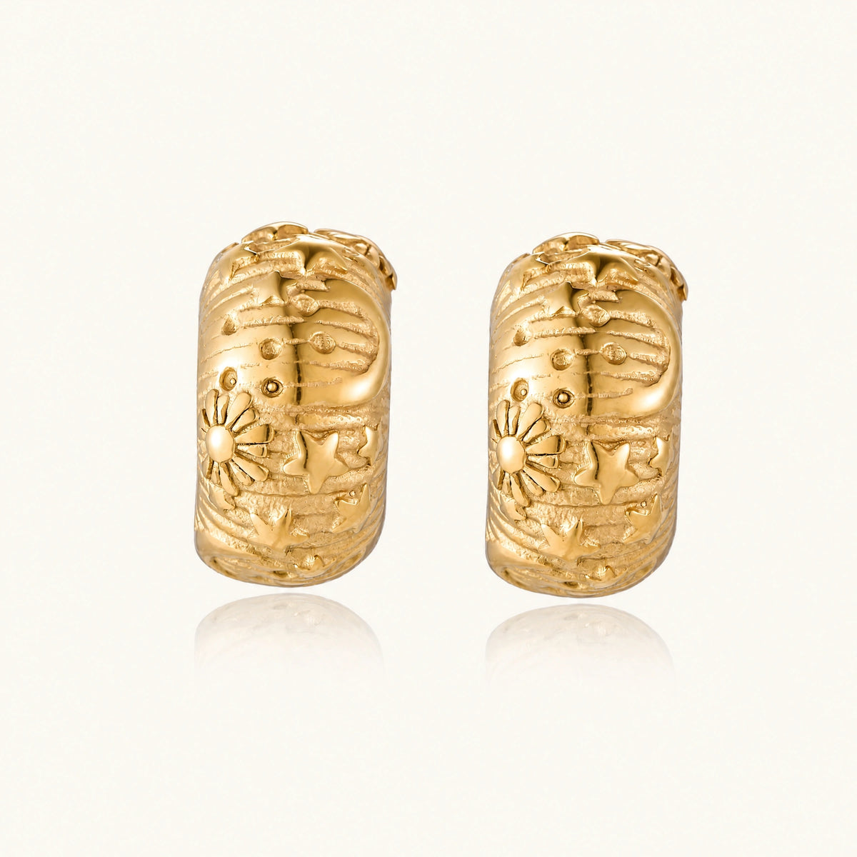 Wide gold hoop earrings with embossed stars and sun motifs on cream background, showing dimensional relief details.
