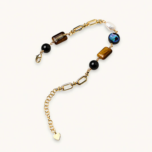 Gold chain bracelet with tiger's eye, obsidian, pearl, and iridescent abalone stones on cream background.